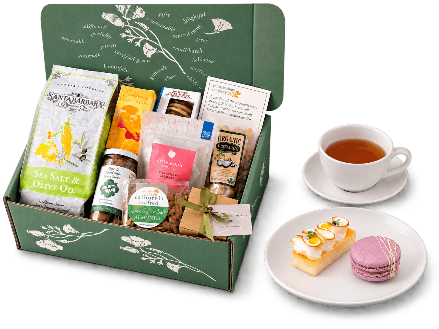 An open green gift box packed with California treats, beside a cup of tea and a plate of pastries.